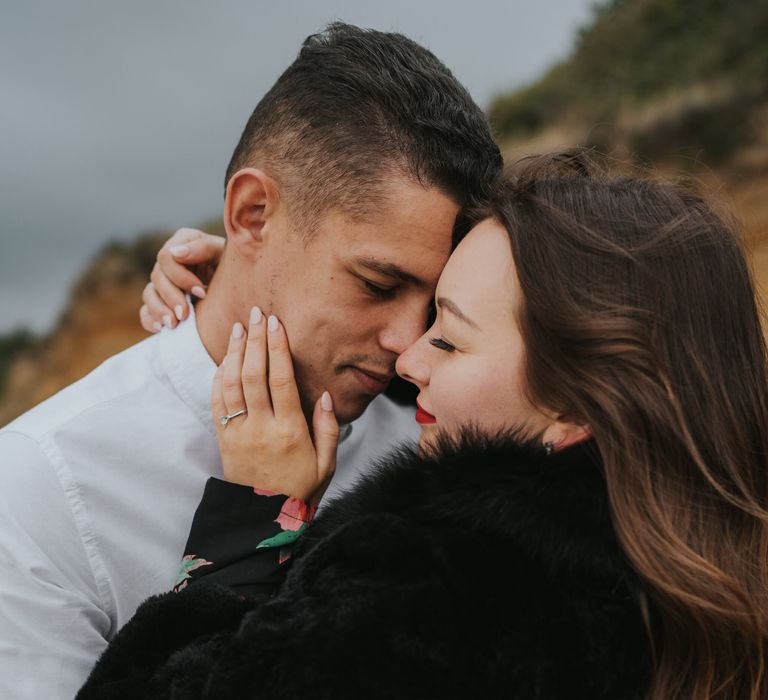 Intimate engagement session photograph with bride-to-be with beige nail polish caressing her groom-to-be's face showing off her diamond engagement ring 