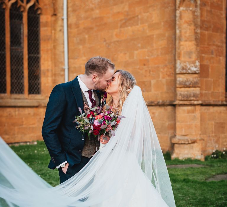 Bride & groom kiss whilst her veil blows in the wind