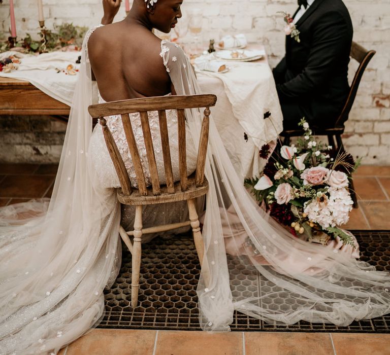 Bride with alopecia sitting at her wedding breakfast in a backless wedding dress with watteau train 