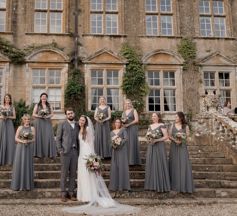 Bride and groom wedding day photography with bridesmaids wearing dark grey bridesmaid dresses outside Brympton House