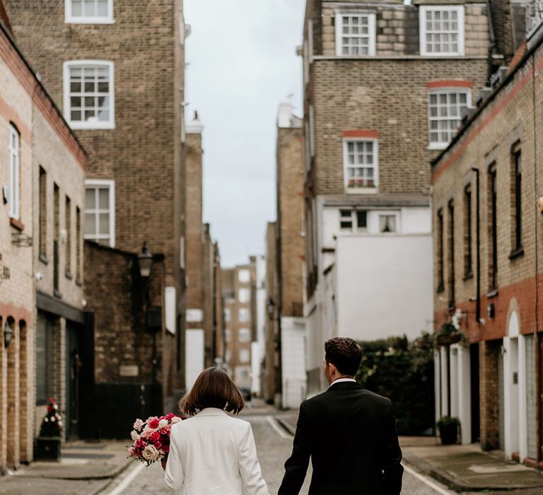 Bride & groom walk away from the camera on their wedding day as they stroll down the street