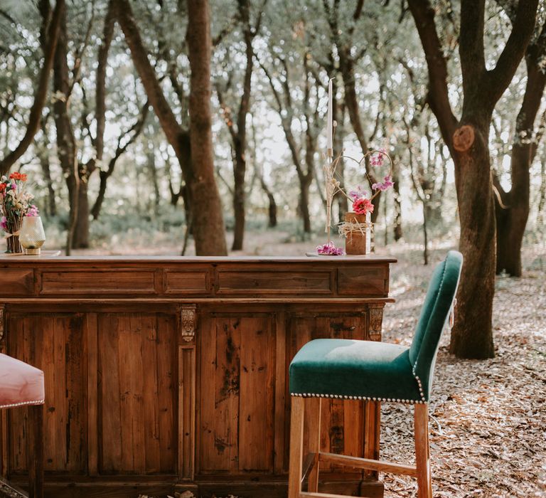 Wooden stand alone bar in woods with two velvet high backed bar stools and pink and red floral decor