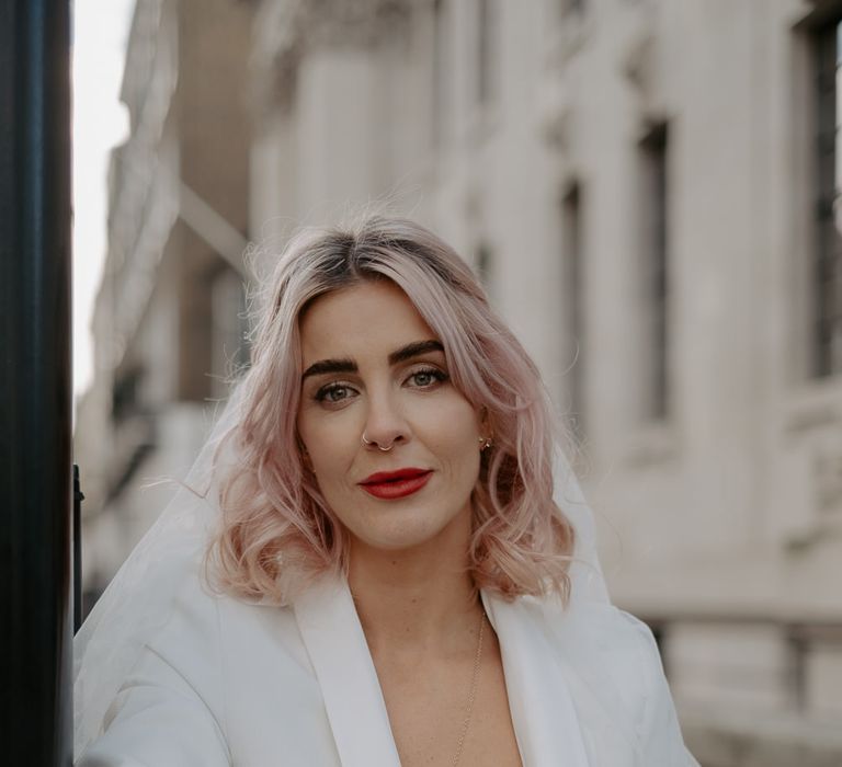 Close up of white bride with pink blonde hair in white suit with red lipstick