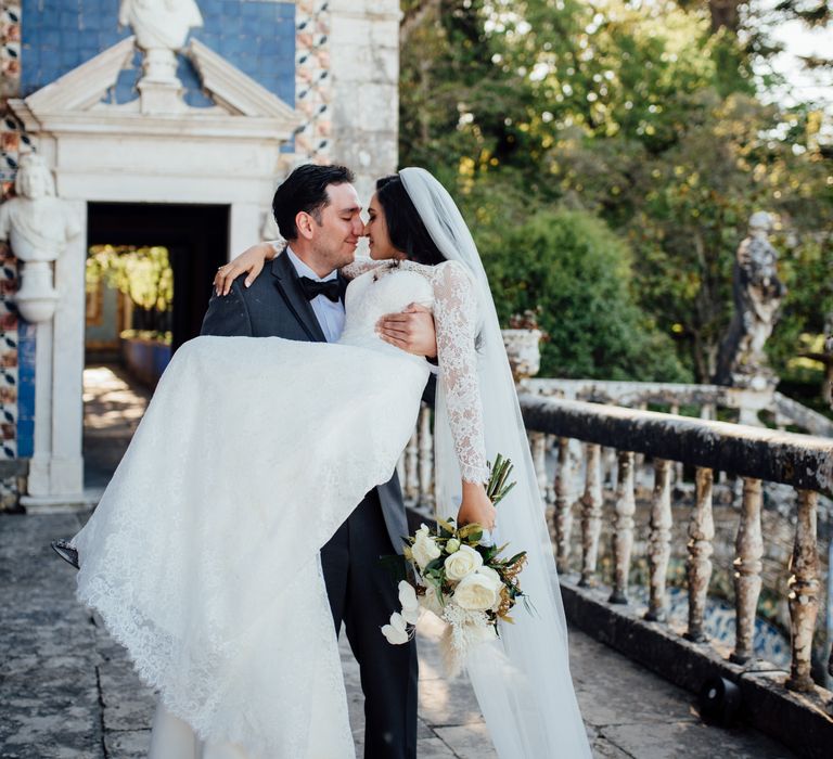 Groom carries his bride outdoors as her dress and veil fall to the floor