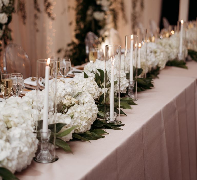 Wedding reception table with green foliage table runner and white pillar candles