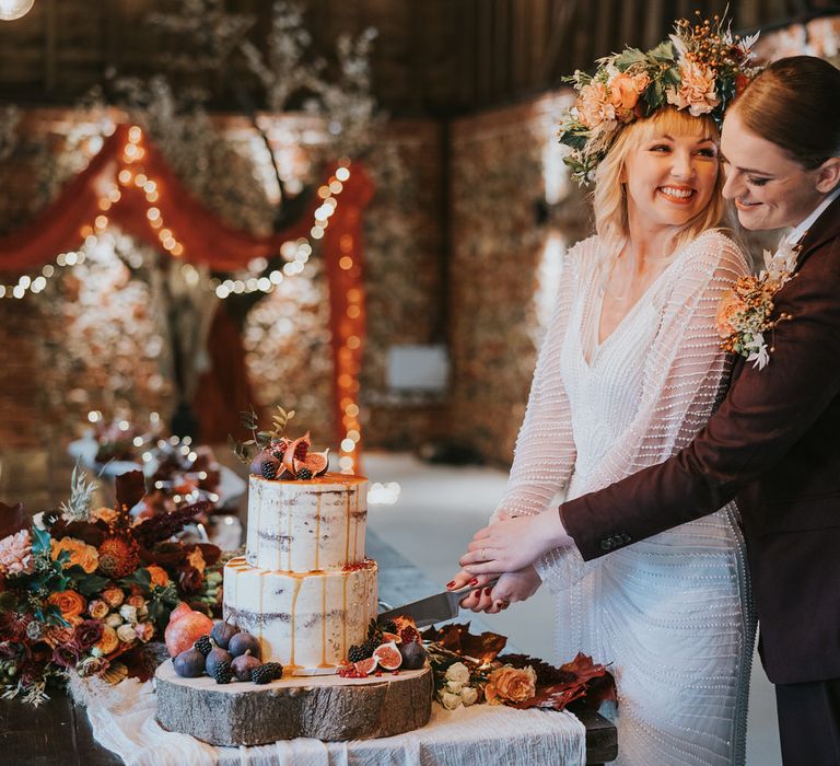 Two brides cutting into rustic two tier naked iced wedding cake for pumpkin spice wedding theme