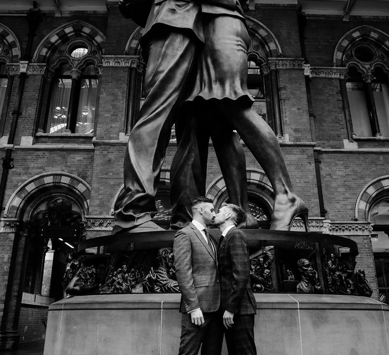 Grooms kiss in front of large statue of couple kissing in London