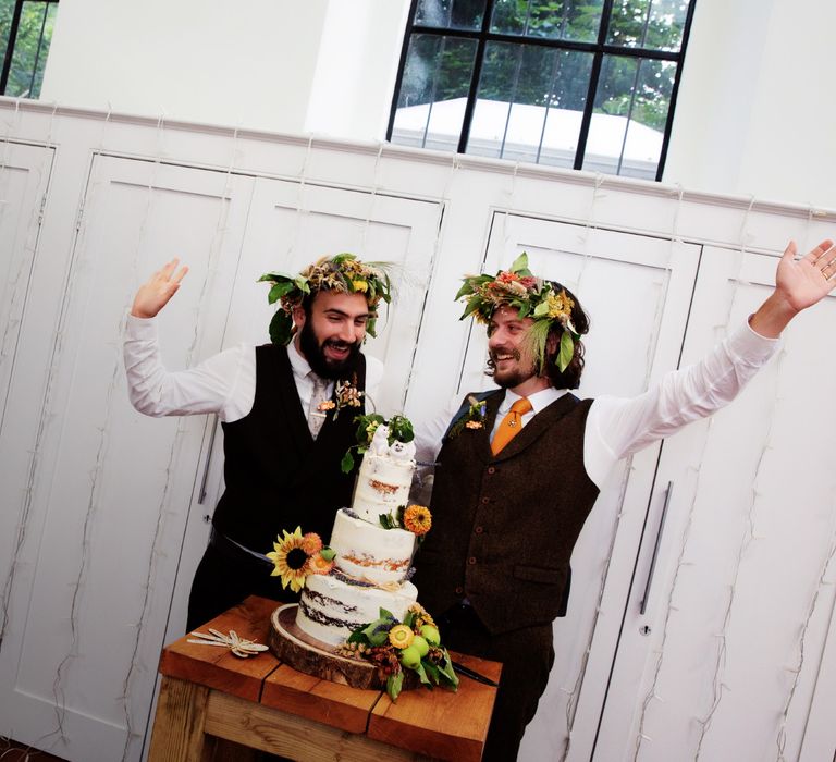 Grooms celebrate in front of naked wedding cake on their wedding day