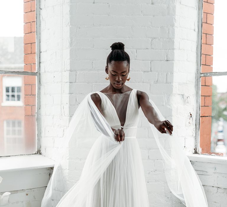 Black bride in a floaty wedding dress with plunging neckline wearing a tulle cape 