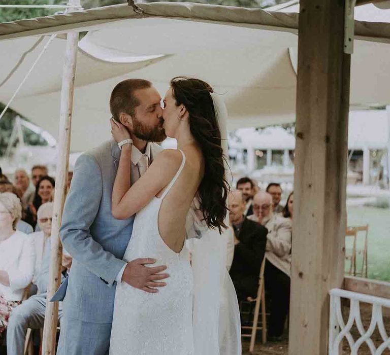 Bride and groom kiss at outdoor wedding ceremony