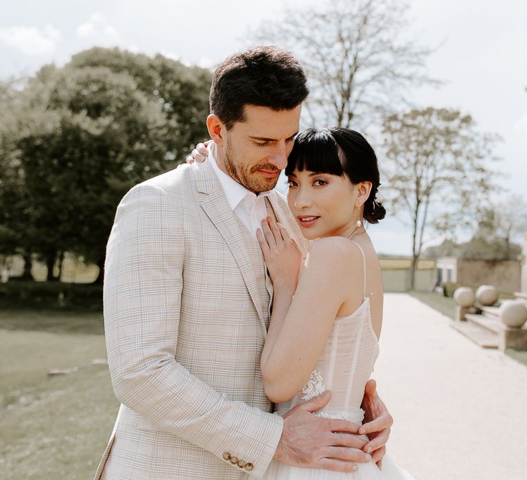 Groom in a beige check suit embracing his South Asian bride with a blunt fringe and bridal bun 