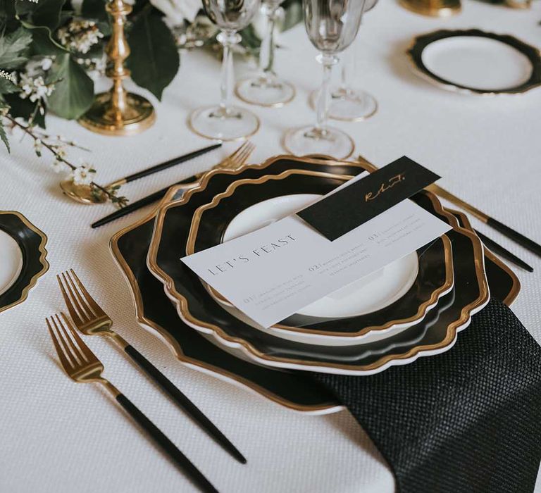 black, white and gold wedding place setting with gold cutlery, black napkin and menu card