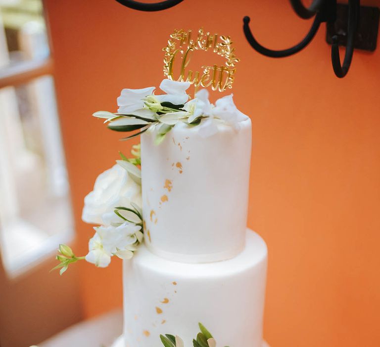 Three tier wedding cake with white frosting and gold decoration complete with white roses 