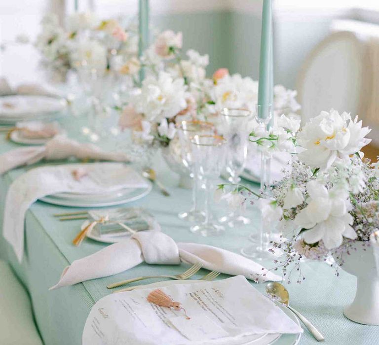 pastel tablescape decor with pale green tablecloth and taper candles and white tableware 