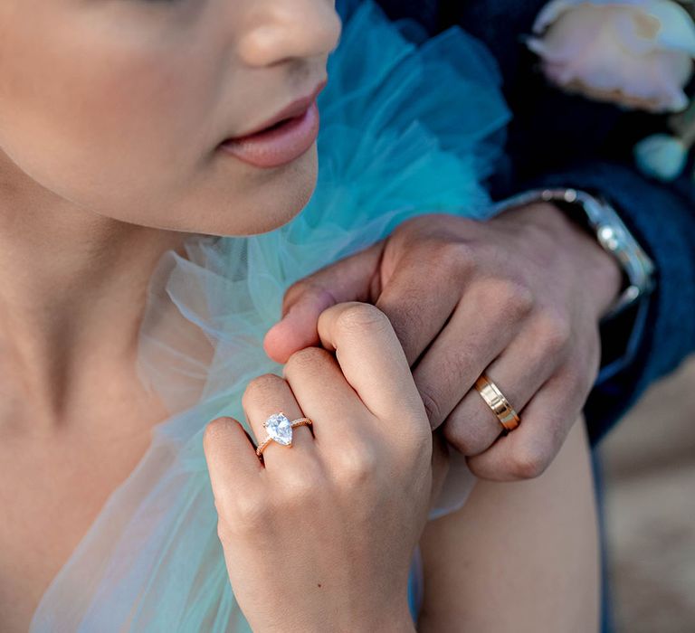 Groom with a gold wedding band and bride with a rose gold pear shape diamond engagement ring holding hands 