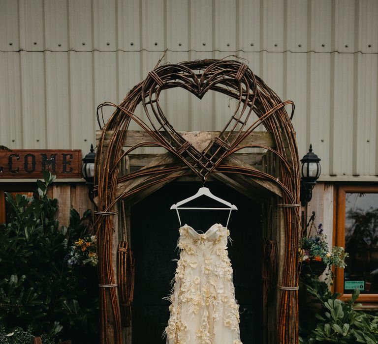 Applique feather wedding dress with cami straps and tulle hanging in doorway at rustic farm wedding