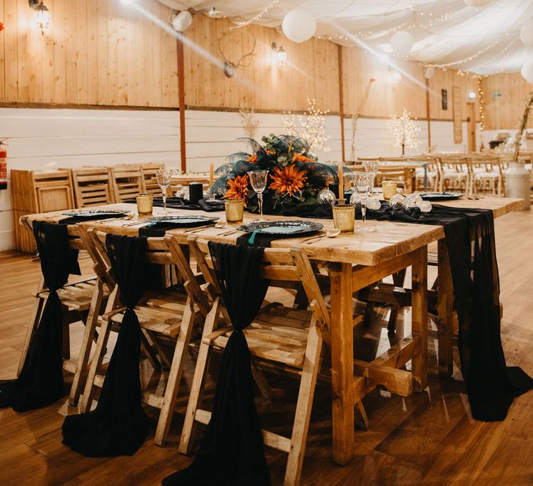 Rustic wedding reception with wooden tables, chairs and fairy lights and blue and orange florals for Wellbeing Farm wedding in Lancashire