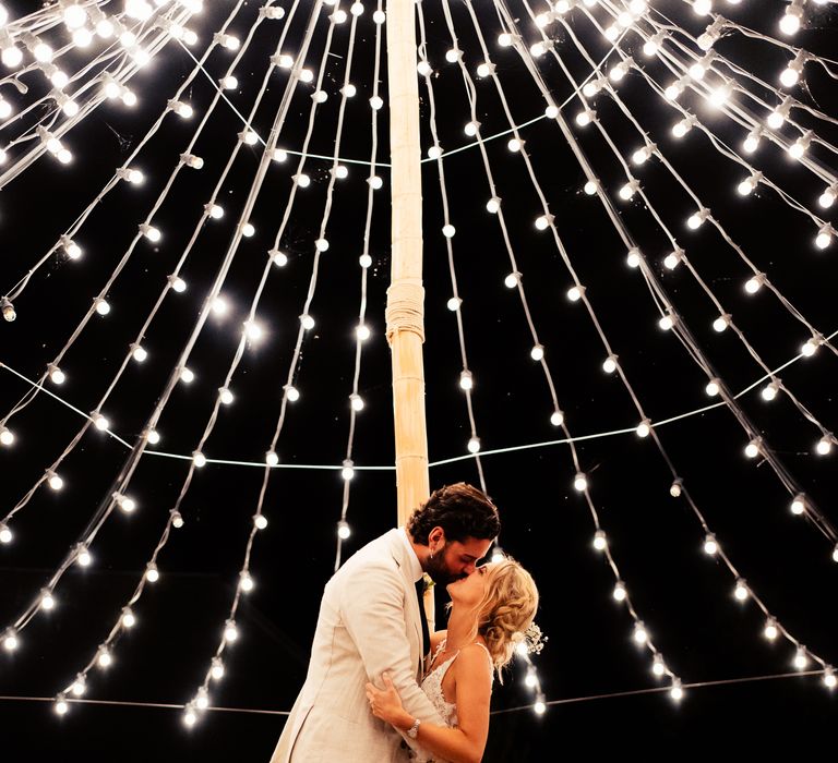 Bride and groom kissing in the courtyard at Preston Court under canopy of festoon lights 