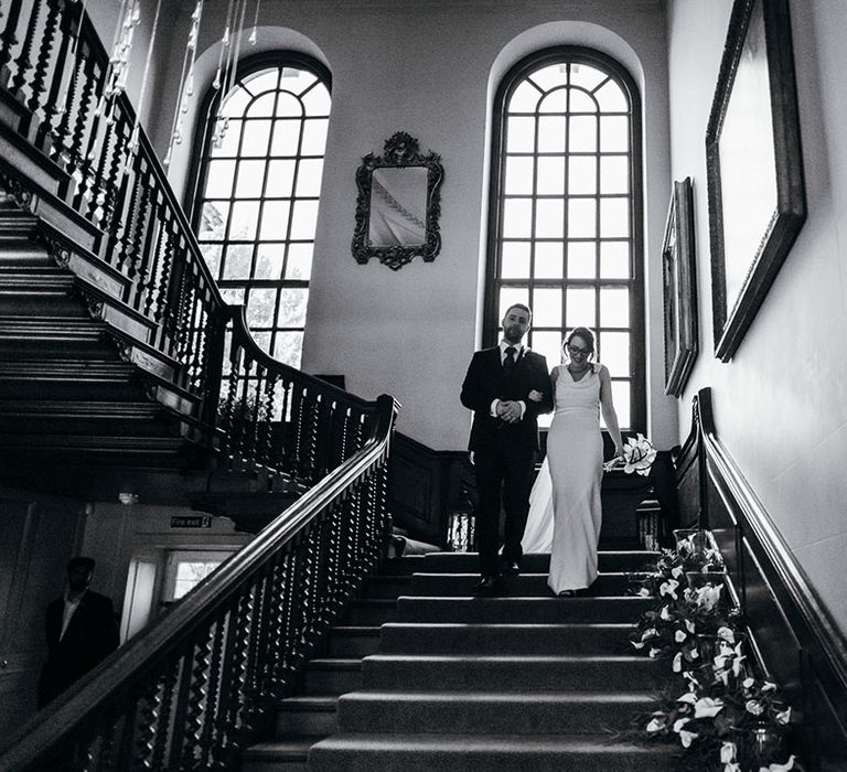 Bride & groom walk down stairs with one another as they link arms