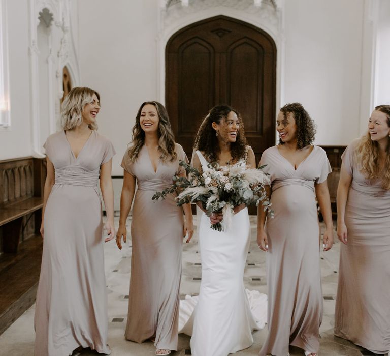 Bride stands with her bridesmaids who wear neutral coloured gowns V-necks