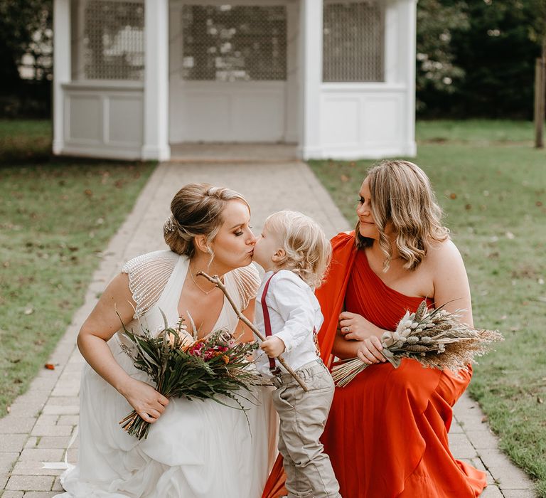 Bride kisses little boy as she kneels with her bridesmaid