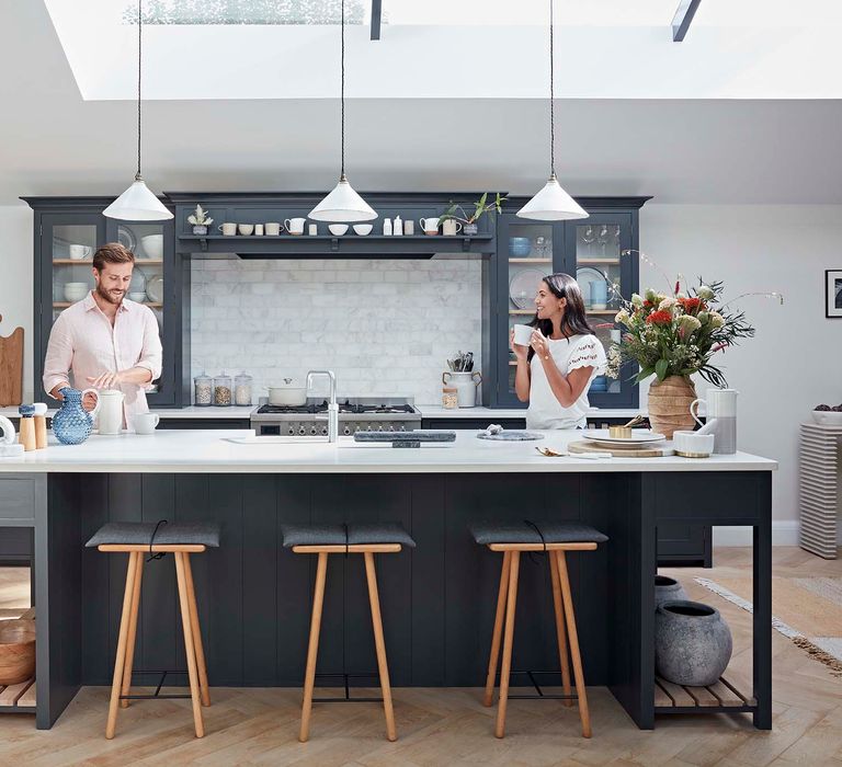 Couple drinking coffess in their grey shaker kitchen with pendant lights, island and stools