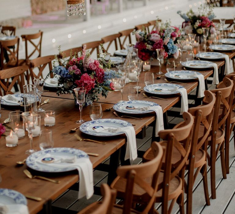 Chandelier hangs above wooden tables complete with bright florals and blue and pink colour scheme 