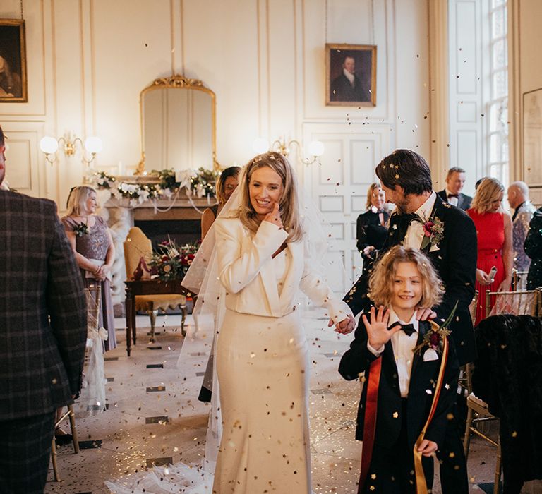 Bride walks down the aisle wearing Nefertiti Crown, Suzanne Neville bridal gown and Zara padded bridal jacket 