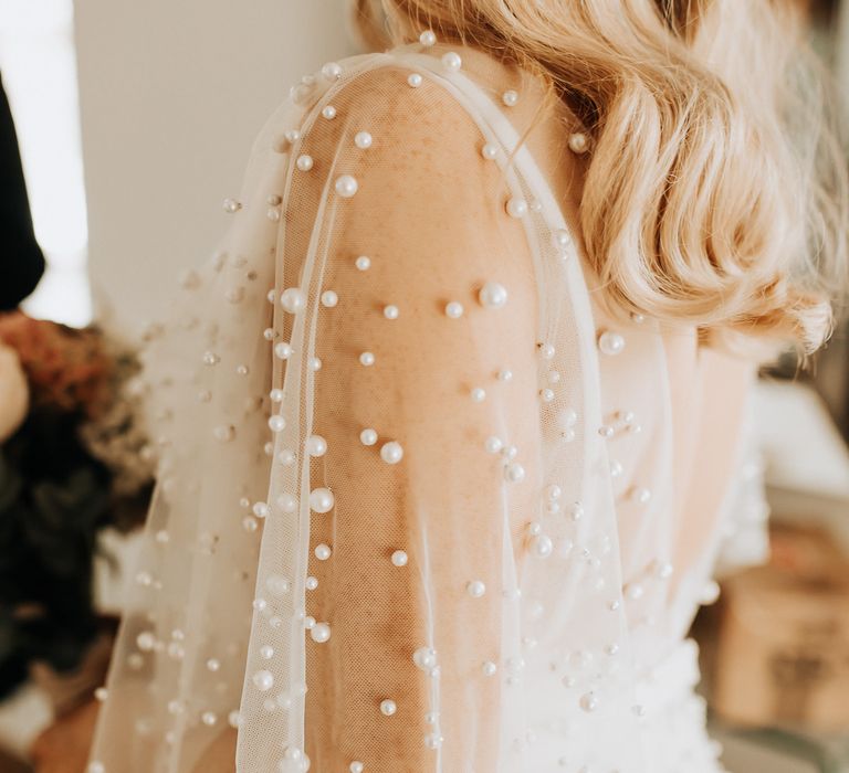 Pearl wedding dress with pearl sleeves worn by bride with curled blonde hair 