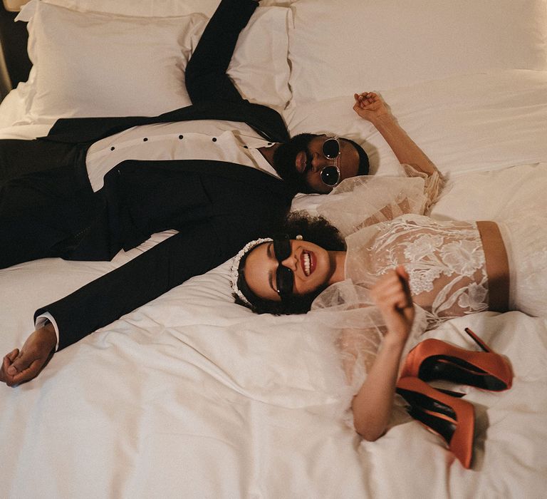 Black bride and groom laying down on the bed at Mayfair Townhouse hotel in sunglasses 