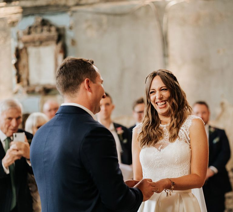 Bride and groom smile at each other at the altar of their wedding as groom slides wedding ring onto bride's finger