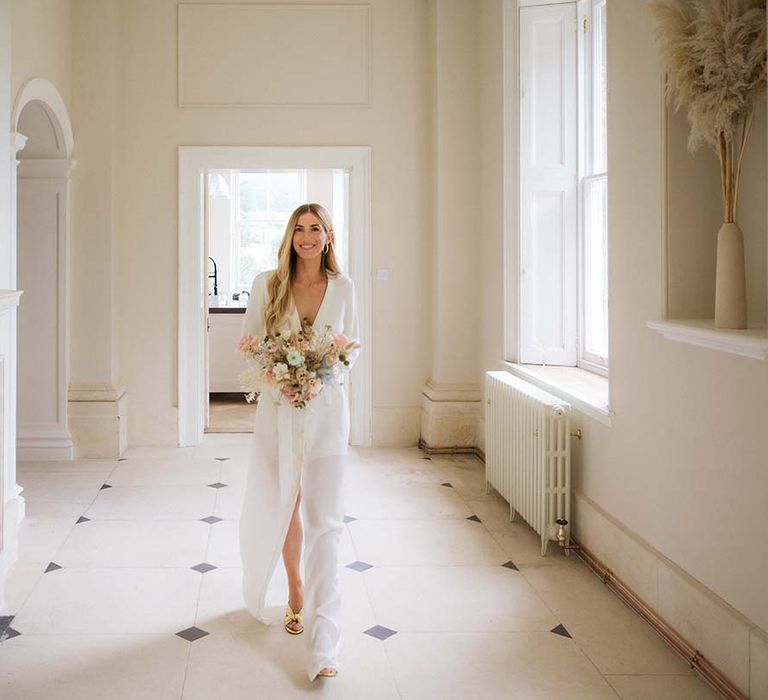 Bride walks in her custom Bon Bride wedding dress with long sleeves and a belt with pastel bouquet