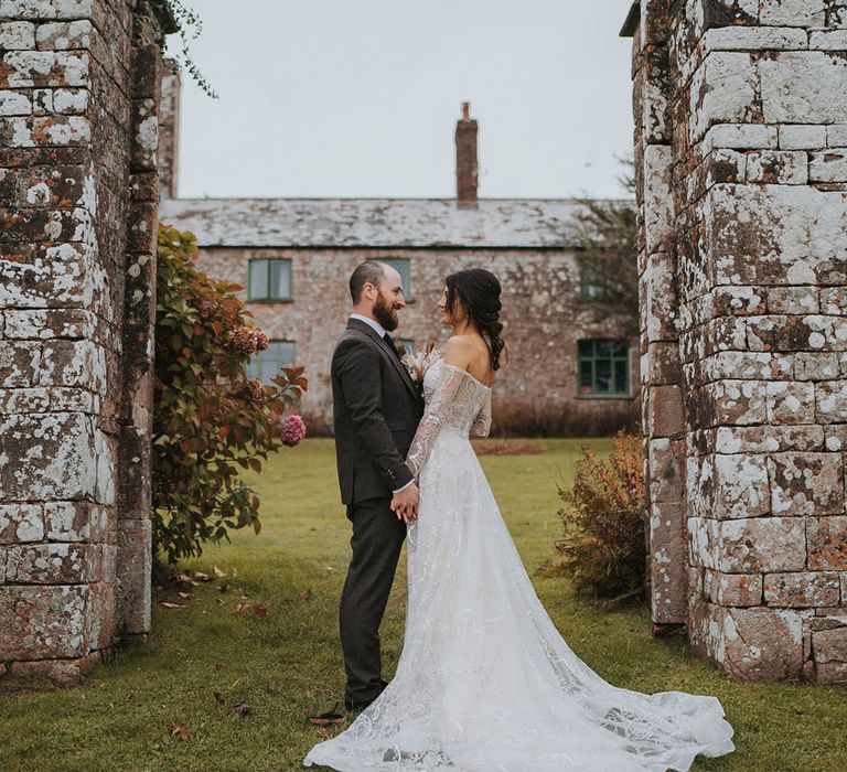 Bride in Zavana Couture wedding dress with long train with groom in three-piece dark grey suit