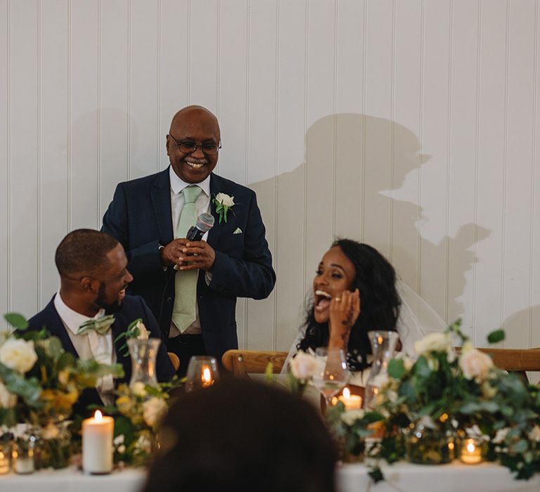 Father of the bride in blue suit and mint green tie and handkerchief give a speech that everyone laughs at 