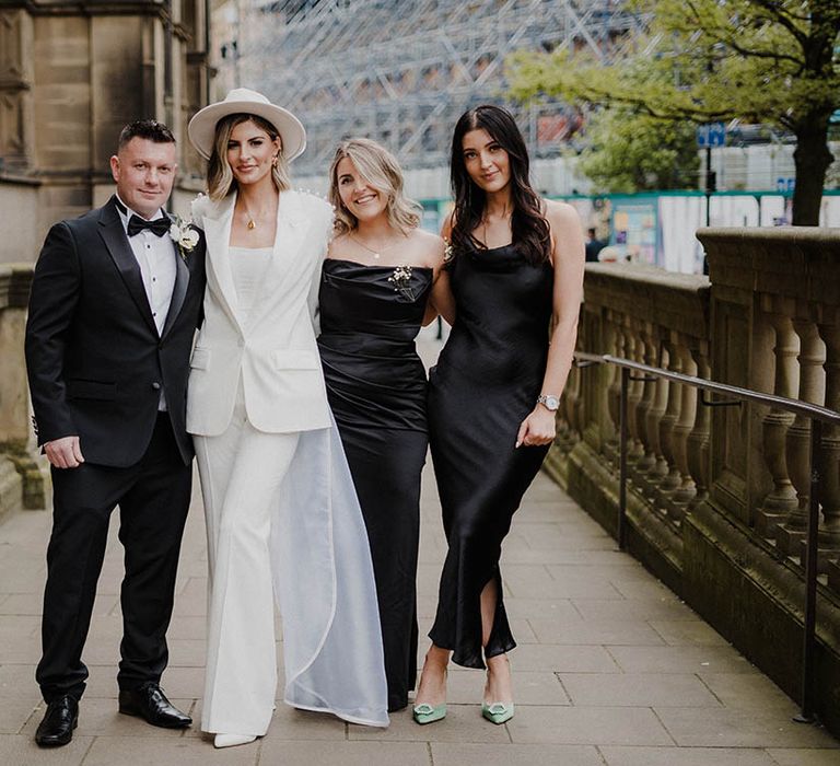 Bride in Nadine Merabi pearl trouser suit with bridal party in black tie and black satin bridesmaid dresses 