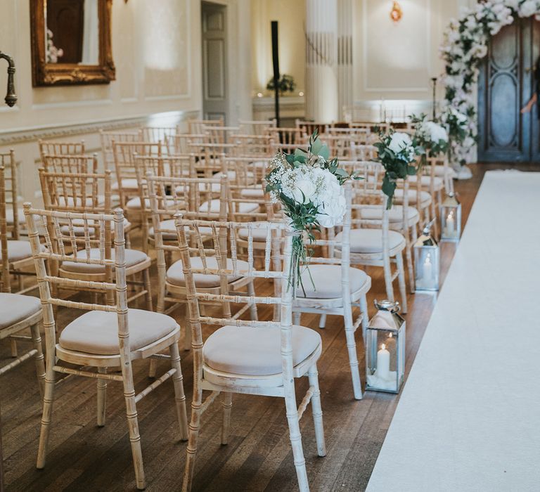 White chairs with silver candle lantern aisle decoration and white roses on the chairs  