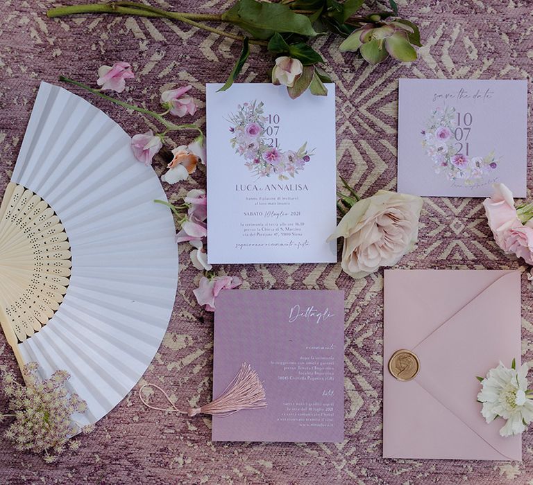 Purple stationery in different shades next to floral decor and fan