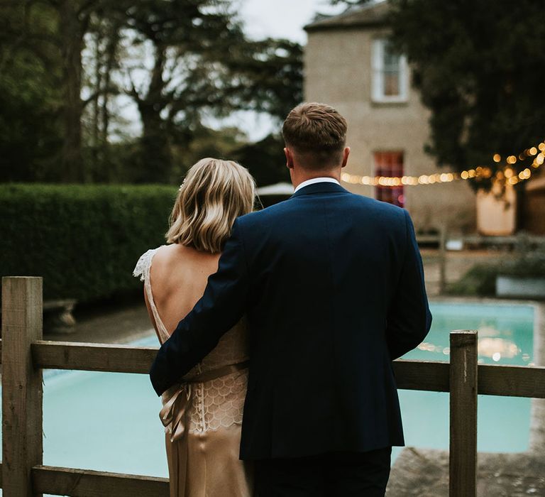 Groom stands with his arm around bride on their wedding day as they stand outdoors at Aswarby Rectory 