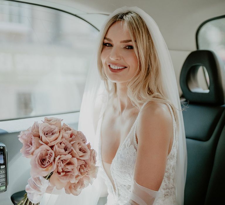 Bride in Made With Love wedding dress carrying pink rose round bouquet in a taxi on the way to the wedding 