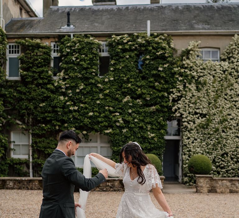 Groom spins his bride around as her wedding dress finished with lace floral embellishment flows around her 