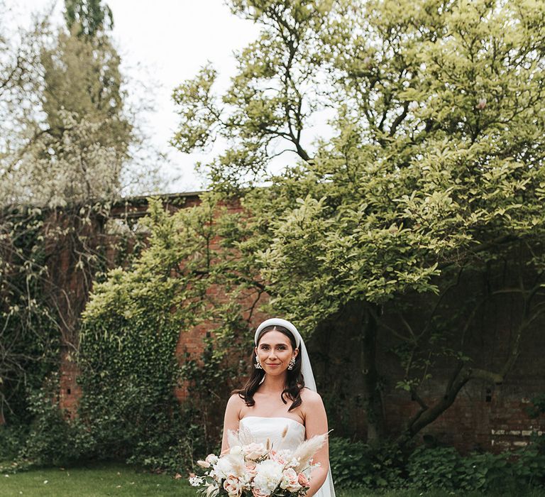 Contemporary bridal look with a strapless pleated Jesus Peiro wedding dress, white chunky headband, pearl earrings, and blue pink bouquet 