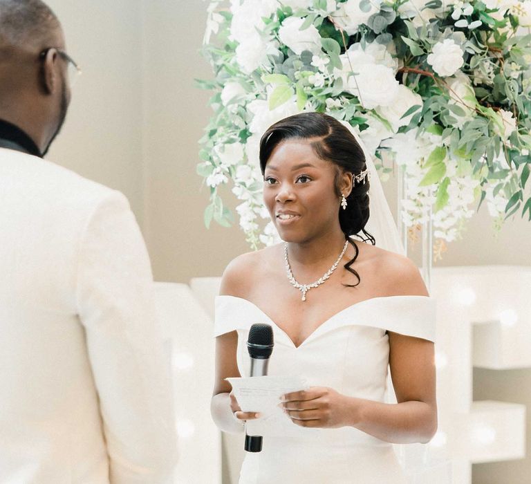 Bride wears fitted off-the-shoulder wedding dress with sweetheart neckline whilst reading her vows at the Edgbaston Park Hotel