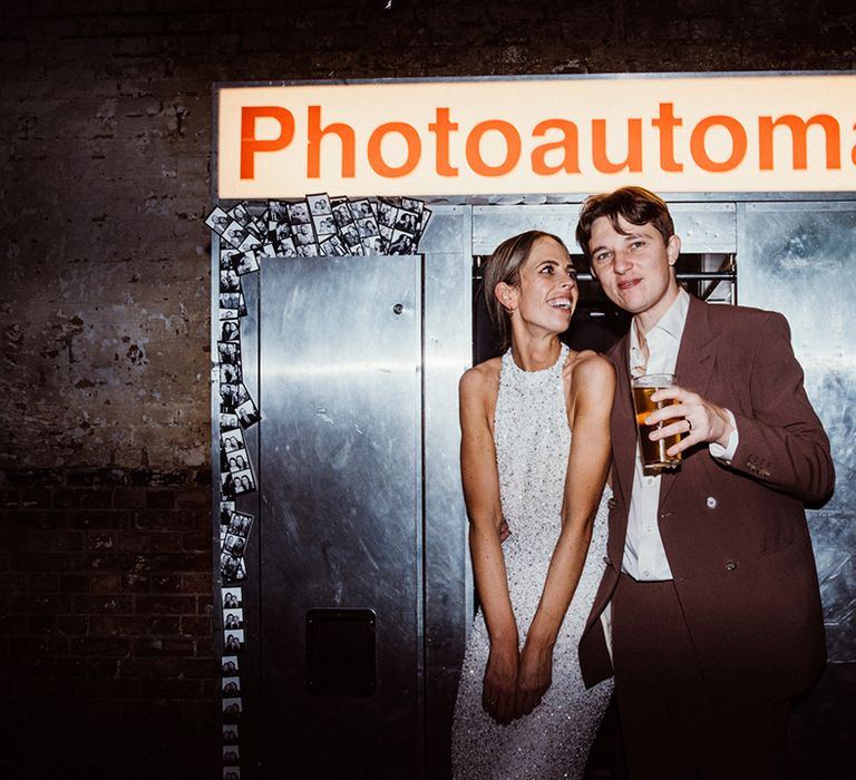 Bride and groom pose together outside of their vintage photoautomat photo booth 