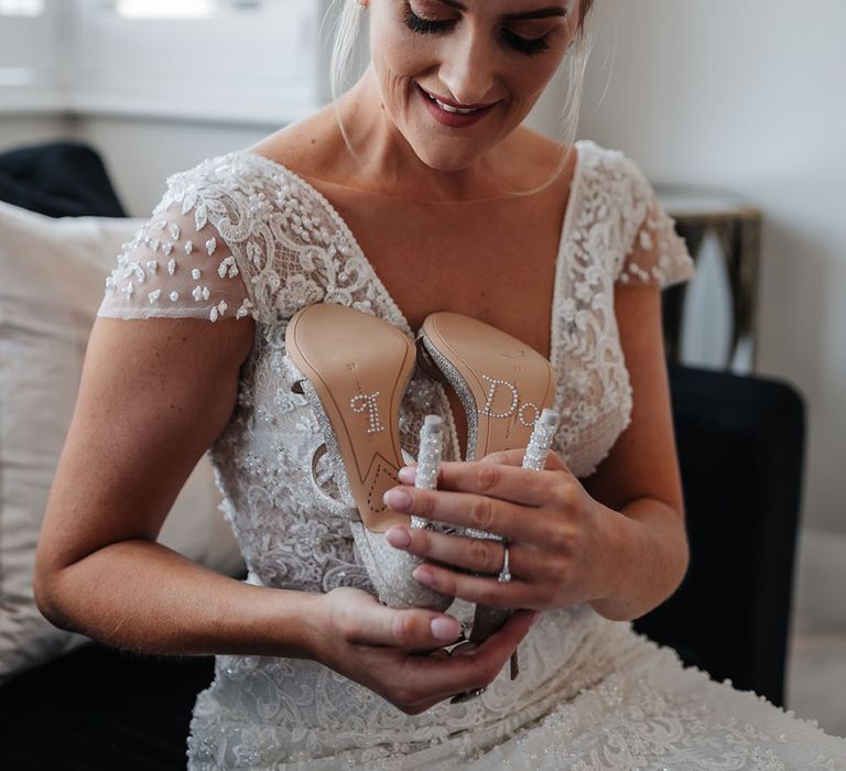 Bride holds up bridal heels complete with 'I Do' pearl embellishment to the soles