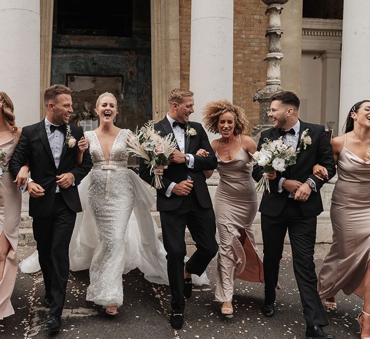 Bride wearing Eva Lendal wedding dress detachable whilst stood with wedding party in black tie and bridesmaids in silk cowl neck spaghetti strap dresses