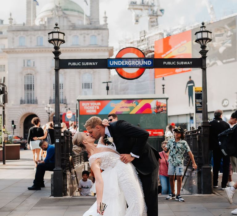 Bride & groom kiss in front of underground station in London on their wedding day 