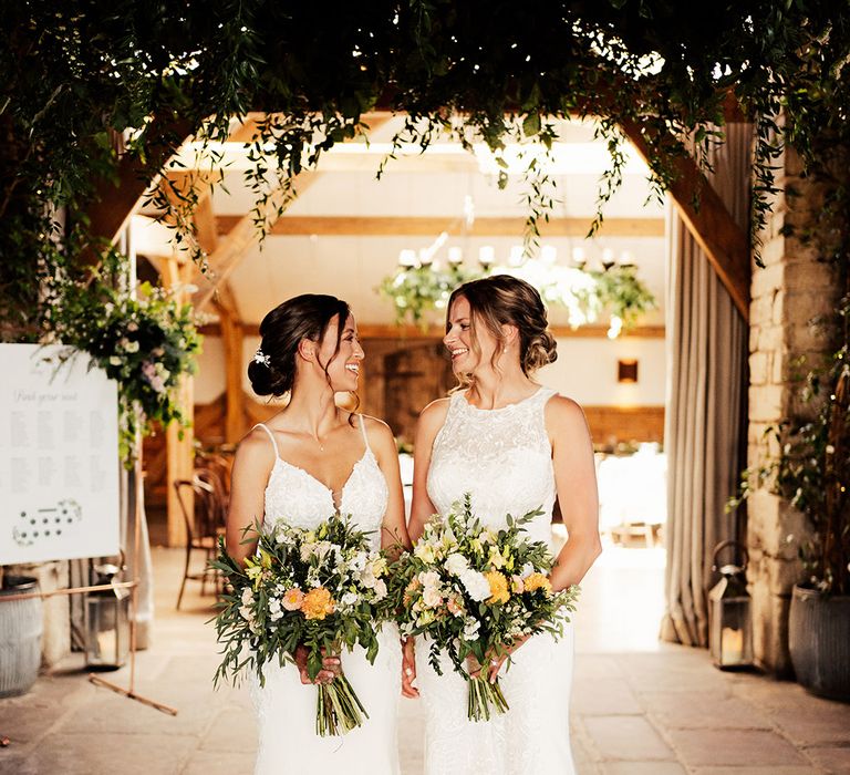 Brides look into each others eyes as they stand in lace fitted wedding dresses