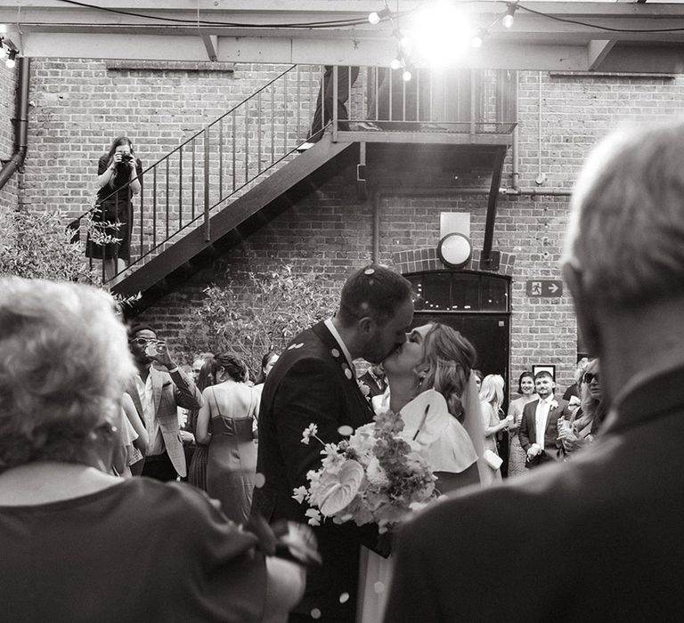 Bride and groom share a kiss as confetti is thrown over them 