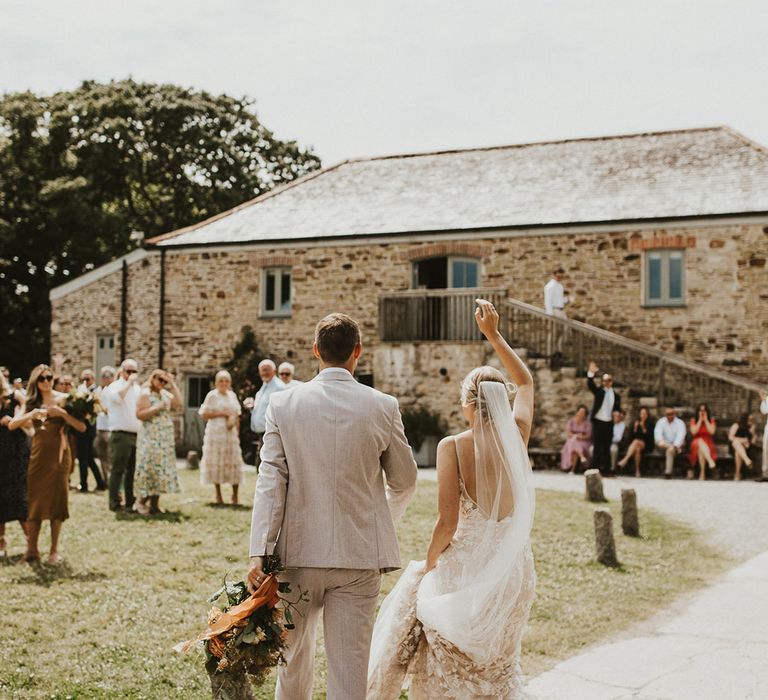 Bride and groom lift up their hands as they enter their outdoor wedding reception 