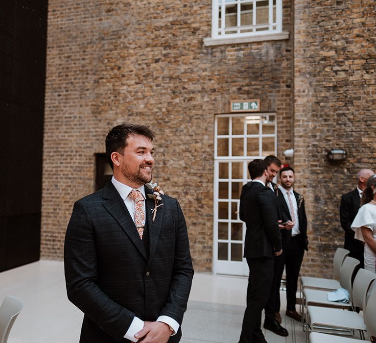 Groom wears three-piece suit with floral tie and floral buttonhole at Hackney Town Hall